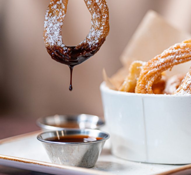 A cinnamon spice churro being dipped into a bowl of Mexican mocha sauce.